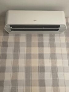 A white Fujitsu wall mounted system against a grey checked wall installed by PRA Air Conditioning
