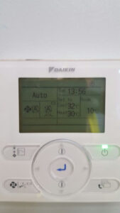 A white Daikin wall mounted Controller with a digital screen to control AC unit and room temperature